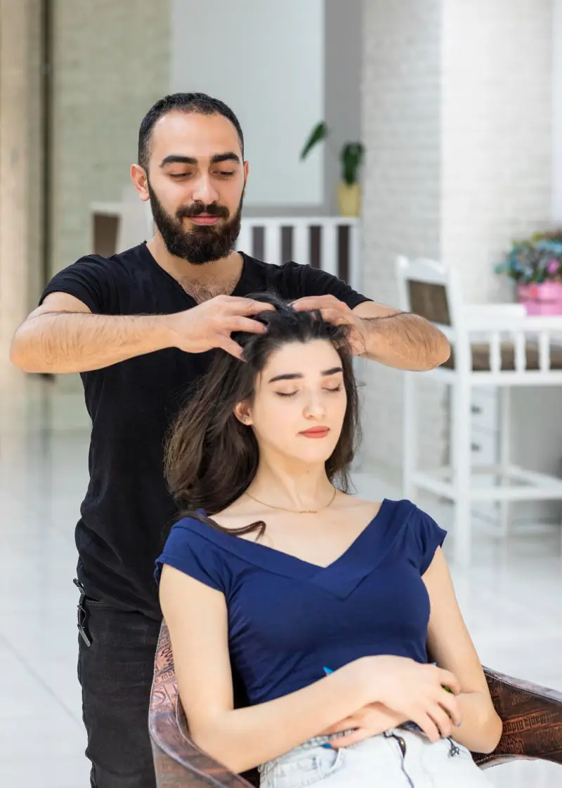 A hairstylist working on a seated woman's hair in a salon-like setting