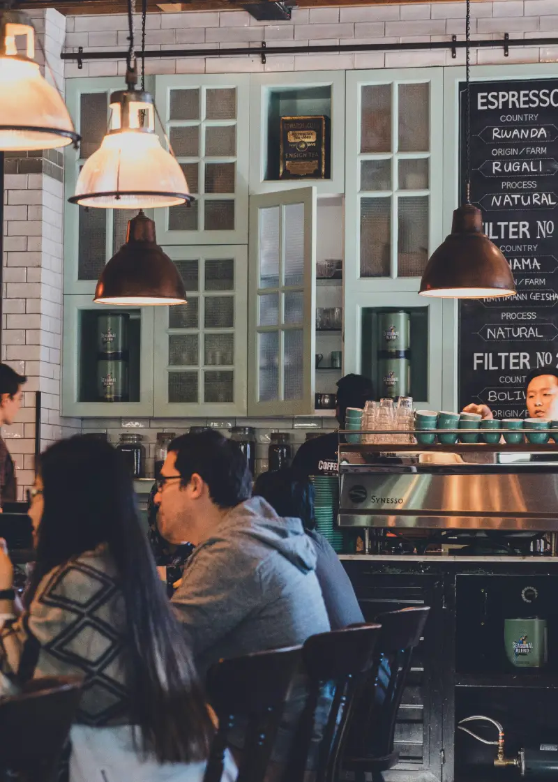 A vibrant café interior featuring patrons enjoying drinks, cozy seating, and a menu highlighting various coffee options. Warm lighting enhances the atmosphere